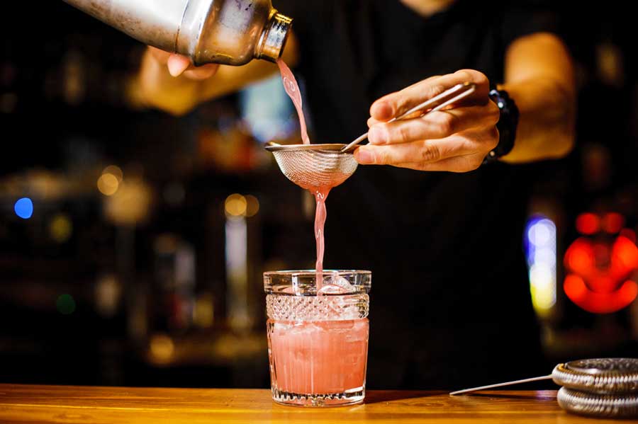 View of a a pink cocktail being pour by the bartender on a glass