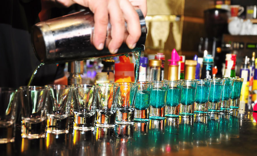 View of shot glasses being poured with liquors by the bartender