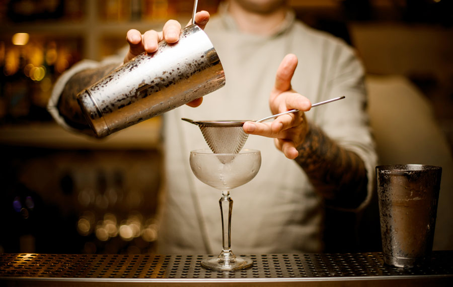 View of a bartender pouring the cocktail from the steel shaker
