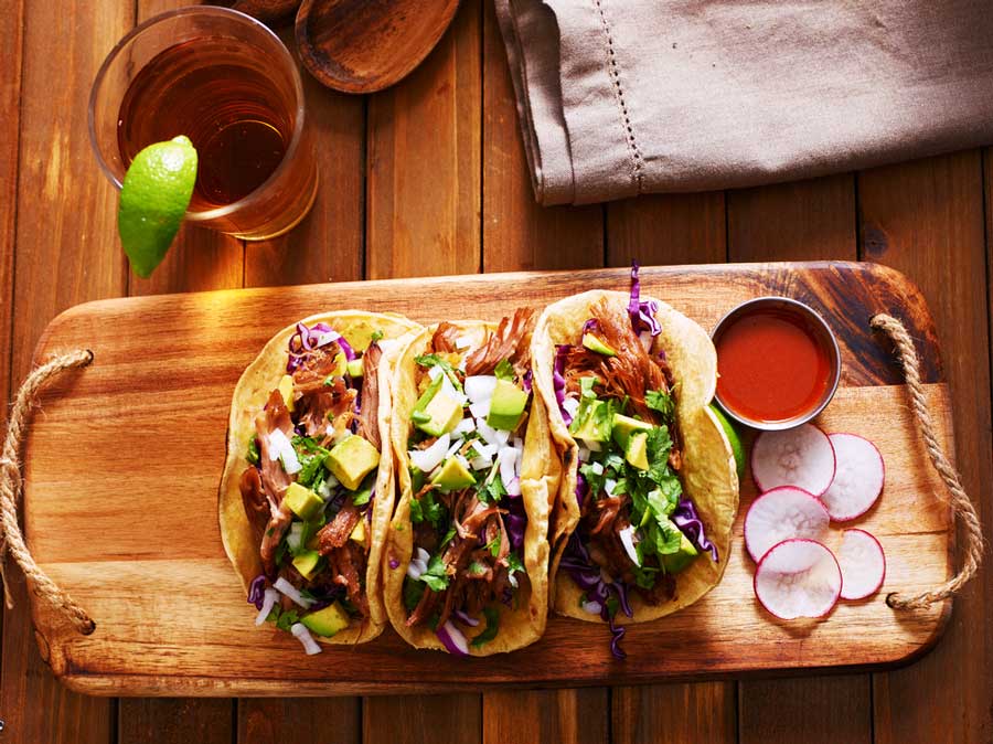 Tacos on a wooden board with sauce and a drink