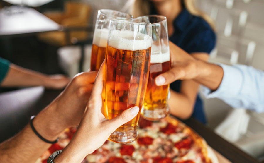 Group of friends tossing with their glass of beer and a pizza on the table