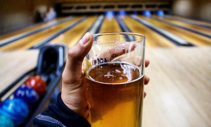 A hand holding a glass of beer and a bowling alley on its background
