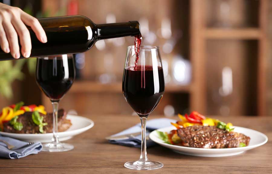 View of a steak on a plate and a bottle of wine being pour on a wine glass