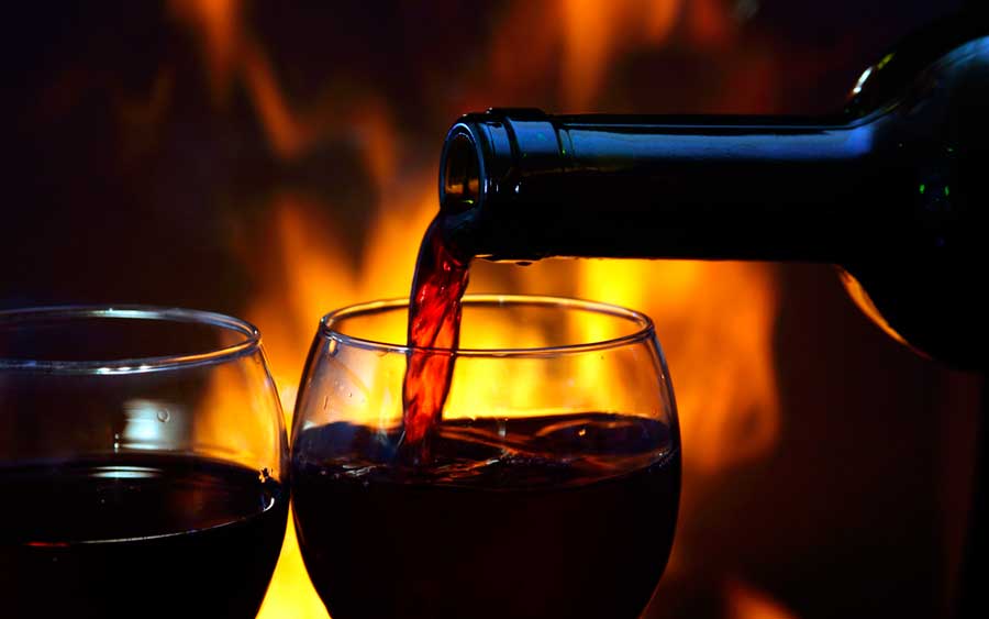 Red wine being poured on a wine glass and a fireplace on the background