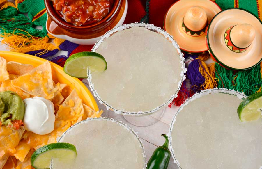 Glasses of cocktail with sugar and lime on its rim and nachos with dip