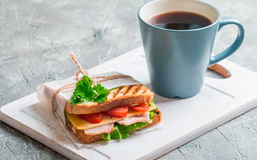 A cup of coffee and a sandwich on a wooden board