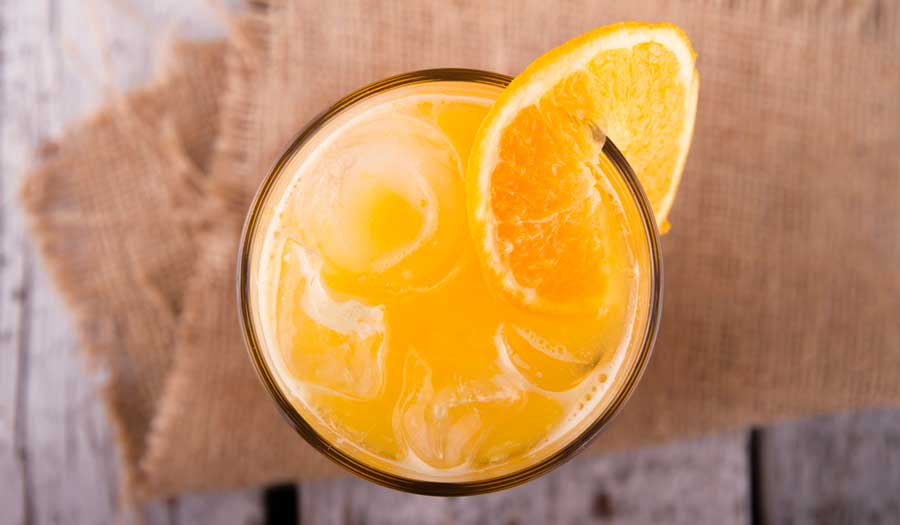 A glass of orange cocktail with orange slice on it